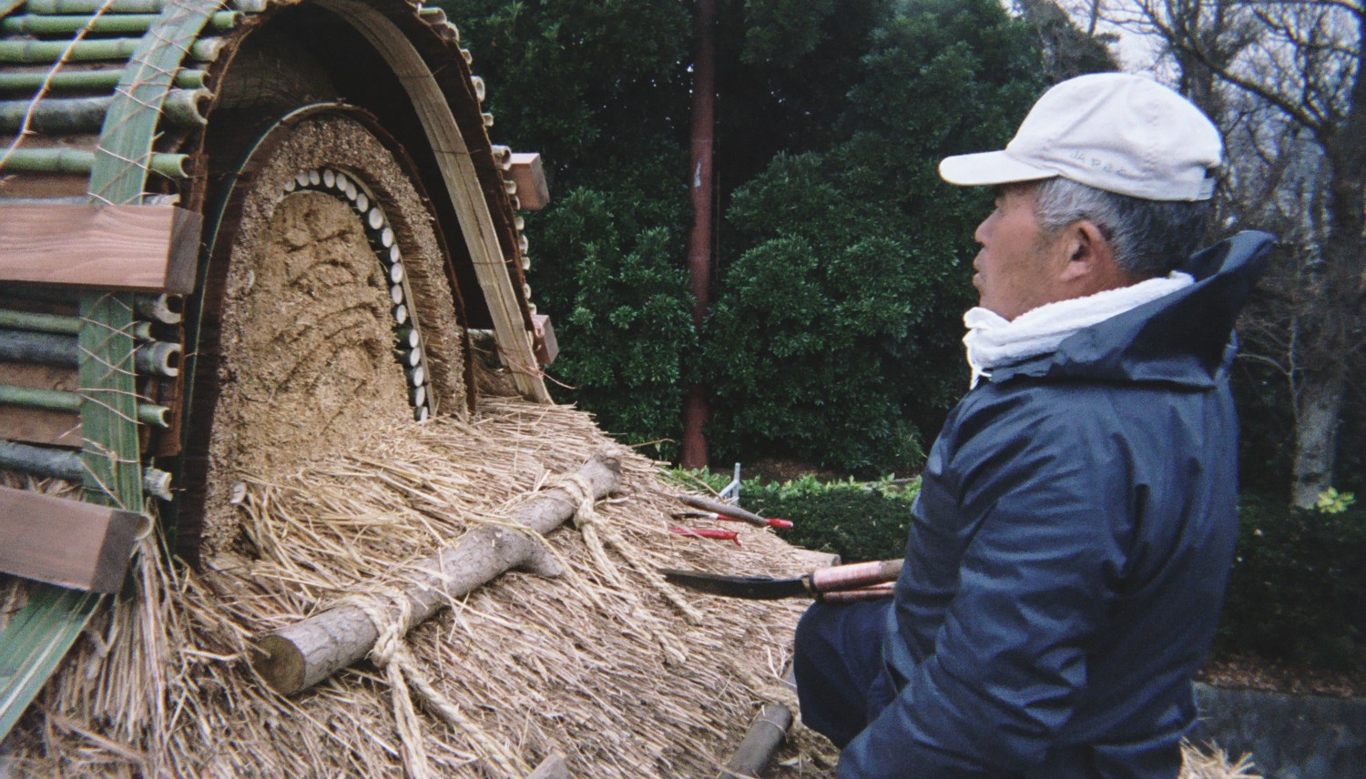 Master craftsman Shigeo Suzuki shaping the ridge detail of a thatched roof in Japan