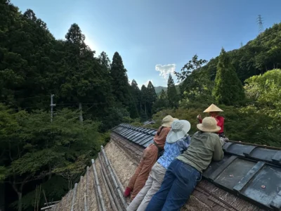 Young apprentice watching Haruo Nishio working on a traditional thatched roof