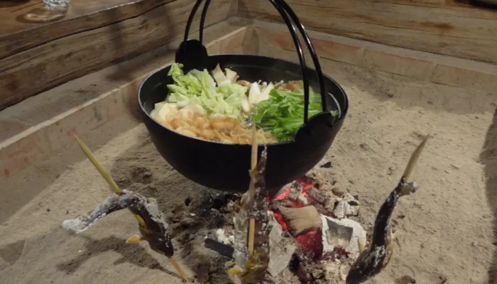 Guests enjoying a hot pot around the irori hearth in a traditional thatched-roof house in Miyama, Kyoto