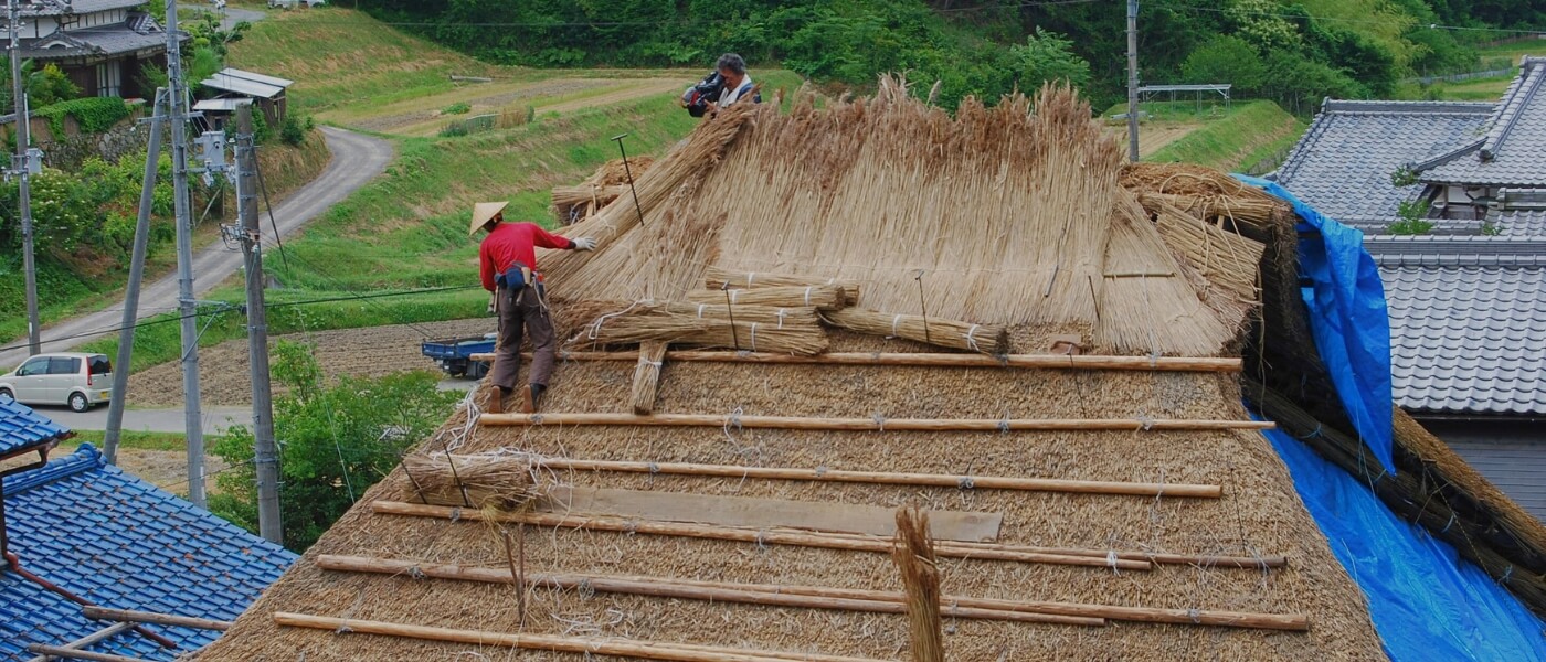 Japanese master thatcher working on the roof of a traditional thatched house
